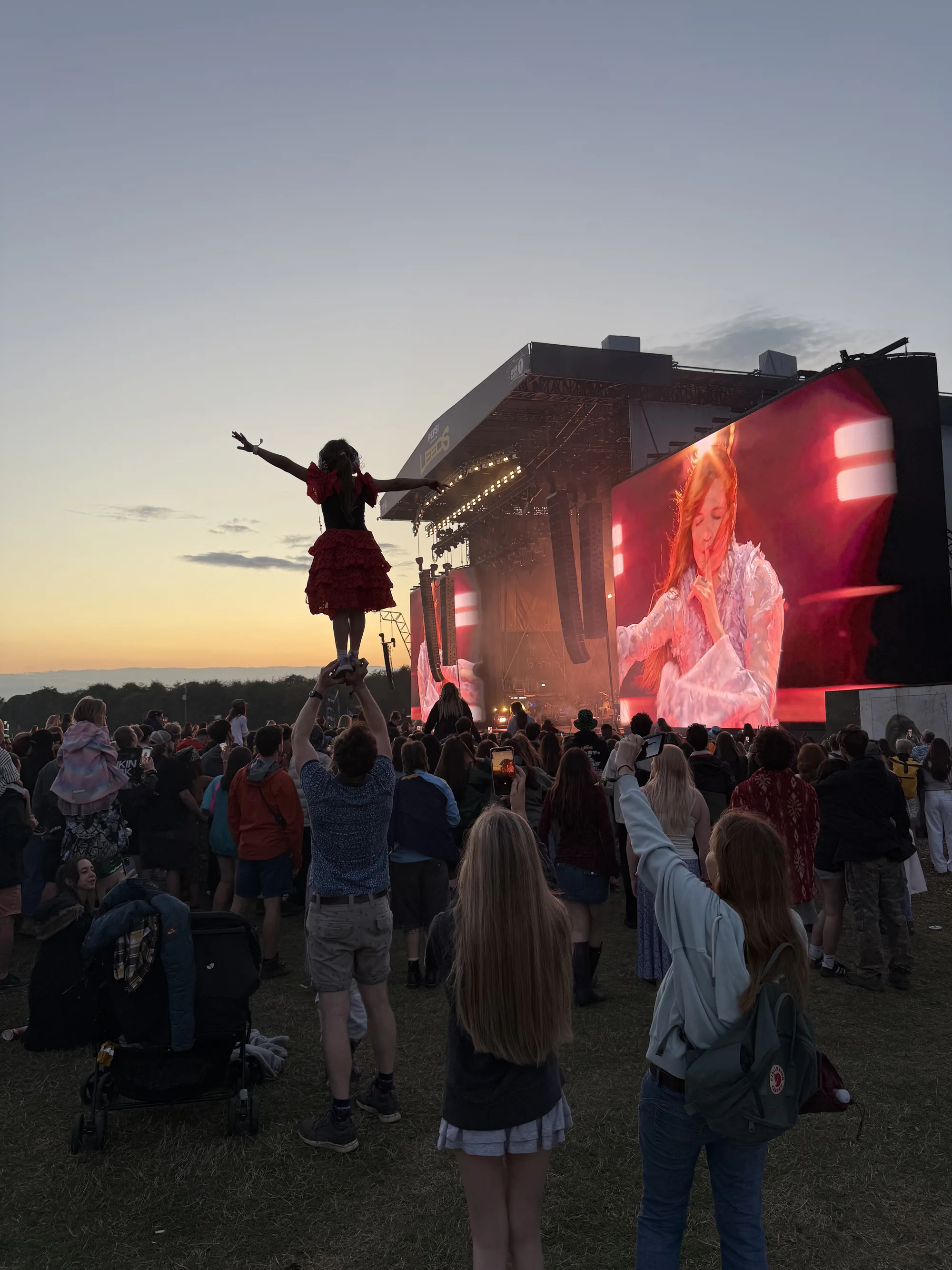 A festivalgoer on someone's shoulders in front of the Leeds Festival stage at sunset